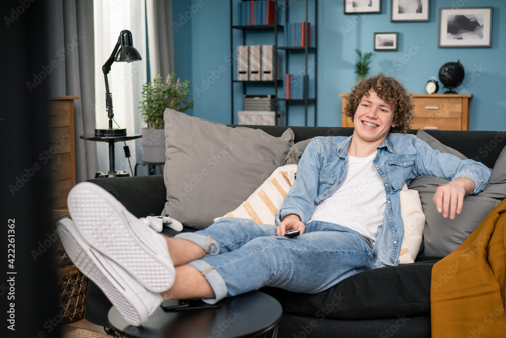 Teen boy sitting on cozy couch and watching comedy on TV laughing with humorous jokes. Teen boy sitting on cozy couch and watching comedy on TV laughing with humorous jokes.