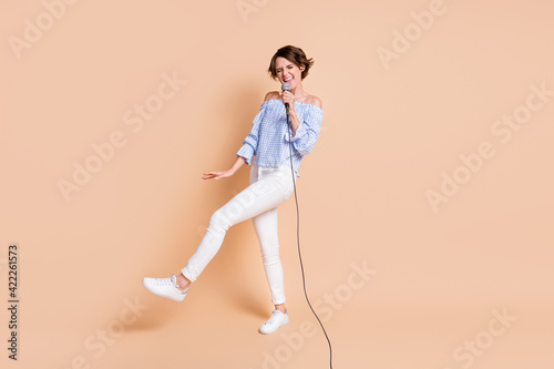 Full size photo of young crazy excited girl happy smile enjoy performance sing microphone karaoke isolated over beige color background