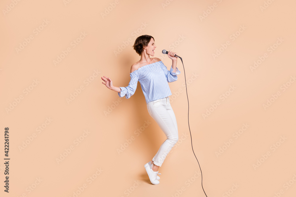 Full size profile side photo of young excited girl sing microphone concert crazy look empty space isolated over beige color background Full size profile side photo of young excited girl sing microphone concert crazy look empty space isolated over beige color background