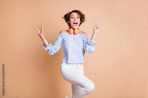 Portrait of lovely amazed cheerful girl showing double v-sign having fun isolated over beige pastel color background