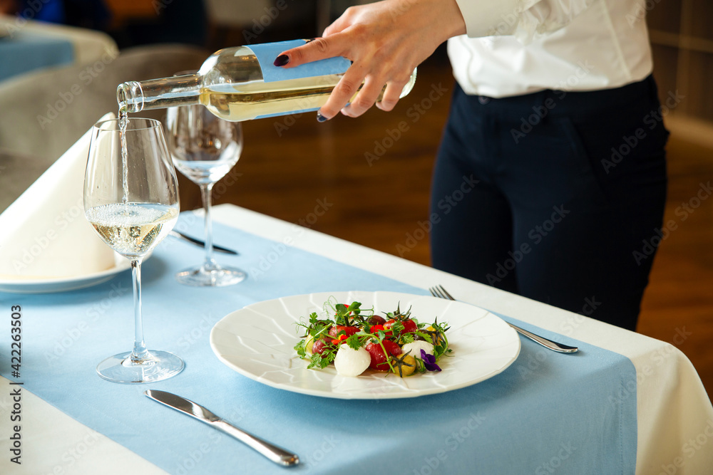Waiter serving the restaurant table with salad and white wine