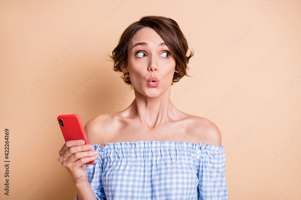 Photo portrait of shocked astonished woman holding phone in one hand isolated on pastel beige colored background Photo portrait of shocked astonished woman holding phone in one hand isolated on pastel beige colored background