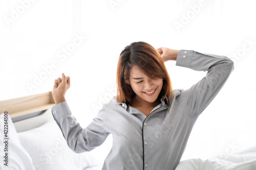 Refreshed young 20s - 30s asian female wakes up in morning stretches seated in bed with morning light. Concept of feel happy and peppy after enough sleeping, greeting new day, ready to start a day