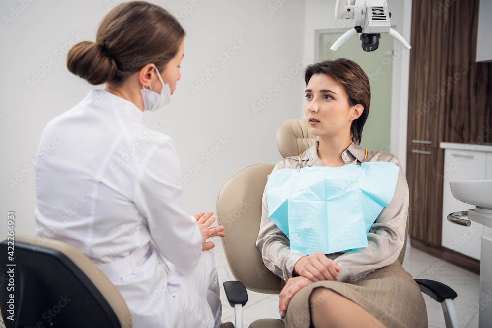 Obraz premium A young woman explaining to her doctor what worries her about her teeth
