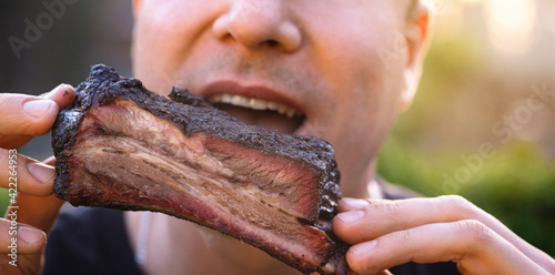 People eat food. A man eats smoked beef ribs BBQ in nature  close-up. 