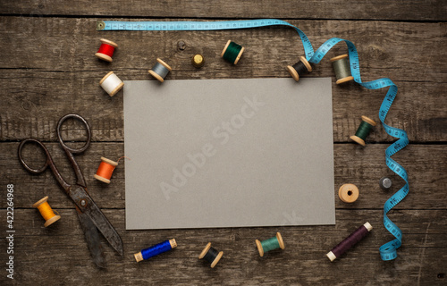 An old style image of cotton reels and other sewing items on a wooden table. Image has been aged to give a retro or vintage style.