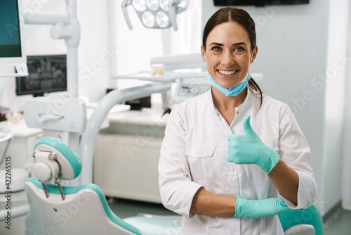 European mid dentist woman showing thumb up in dental clinic photo