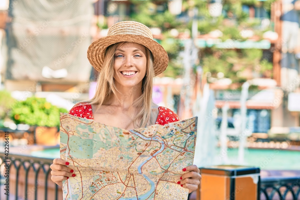 Young blonde tourist woman wearing summer style looking for city route using map at the street.