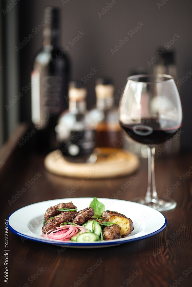 Mini beef cutlets with potato and cucumbers and a glass of red wine