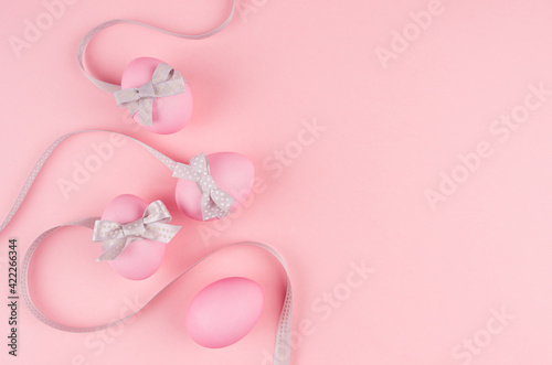 Festive easter background - pink easter eggs with silver bow and curled ribbons as border on pastel pink backdrop.