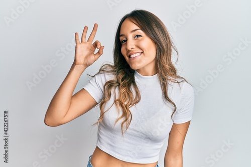 Young brunette woman wearing casual white t shirt smiling positive doing ok sign with hand and fingers. successful expression.