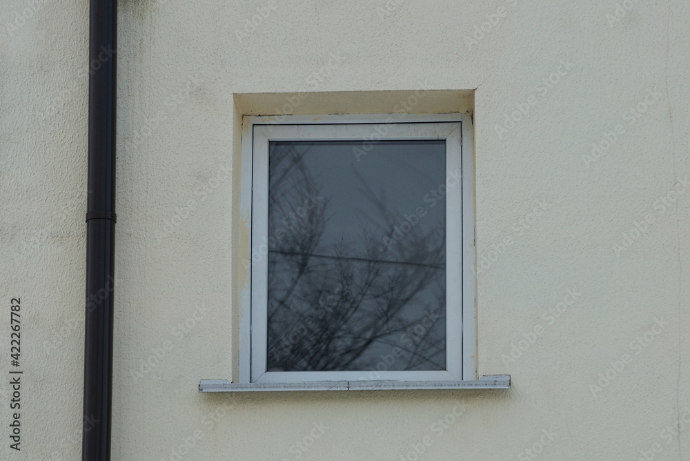 Fototapeta premium one white small window on the gray concrete wall of the building