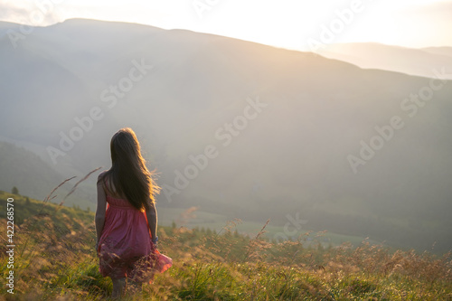 Young woman in red dress walking on grass field on a windy evening in autumn mountains.