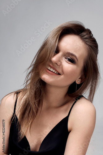 Beautiful young brunette woman smiles and looks at the camera. Dress with straps.