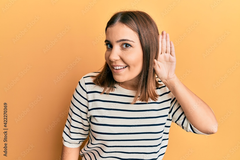 Young beautiful woman wearing casual striped t shirt smiling with hand over ear listening and hearing to rumor or gossip. deafness concept. Young beautiful woman wearing casual striped t shirt smiling with hand over ear listening and hearing to rumor or gossip. deafness concept.