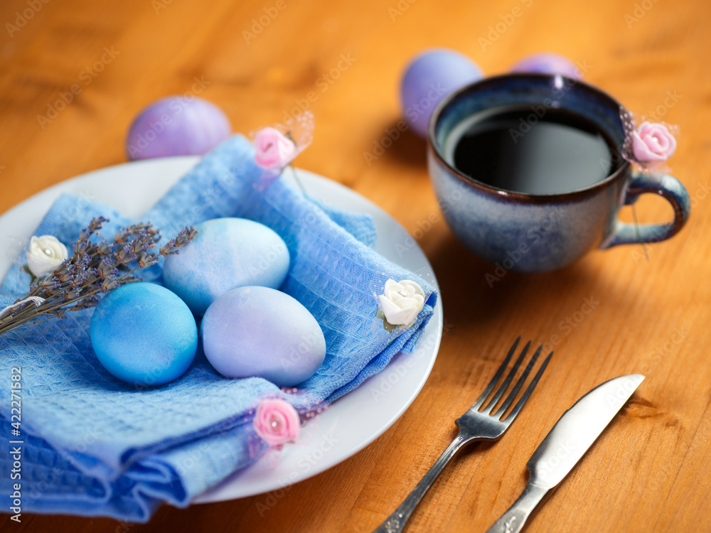 Easter eggs in a white plate, painted with pastel colors. A cup of black coffee on a wooden table. Easter eggs in a white plate, painted with pastel colors. A cup of black coffee on a wooden table.