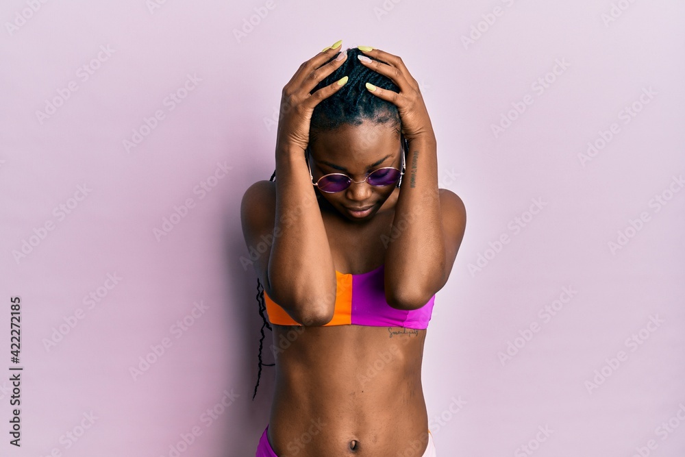 Young african american woman wearing bikini and sunglasses suffering from headache desperate and stressed because pain and migraine. hands on head.