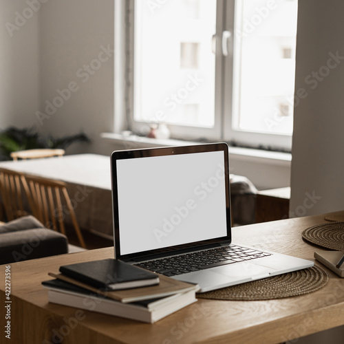 Laptop with blank copy space screen on table with notebooks on wooden table. Minimalist home office workspace. Mockup template.