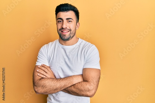 Young hispanic man wearing casual white t shirt happy face smiling with crossed arms looking at the camera. positive person.