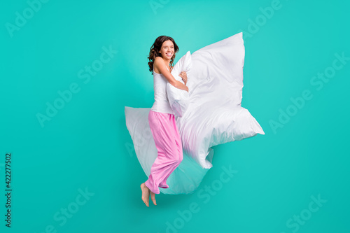 Full length photo of shiny charming young woman sleepwear jumping embracing pillow isolated turquoise color background