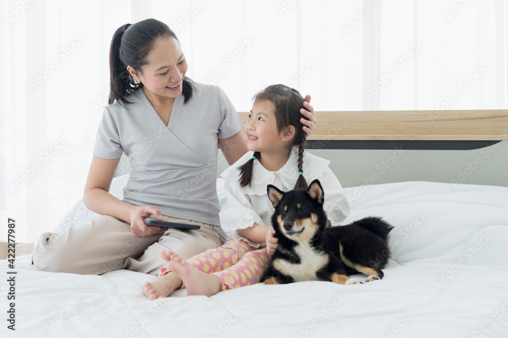 Mom and baby are using a tablet computer in bed with a black Shiba Inu. The Shiba Inu is the national dog of Japan. Mom and baby are using a tablet computer in bed with a black Shiba Inu. The Shiba Inu is the national dog of Japan.