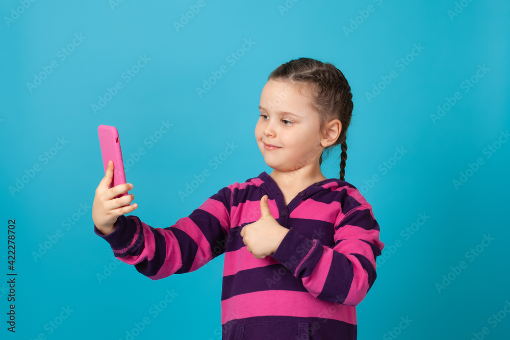 close-up portrait of a smiling girl with pigtails talking on a phone video chat and giving a thumbs up, isolated on a blue background. close-up portrait of a smiling girl with pigtails talking on a phone video chat and giving a thumbs up, isolated on a blue background.