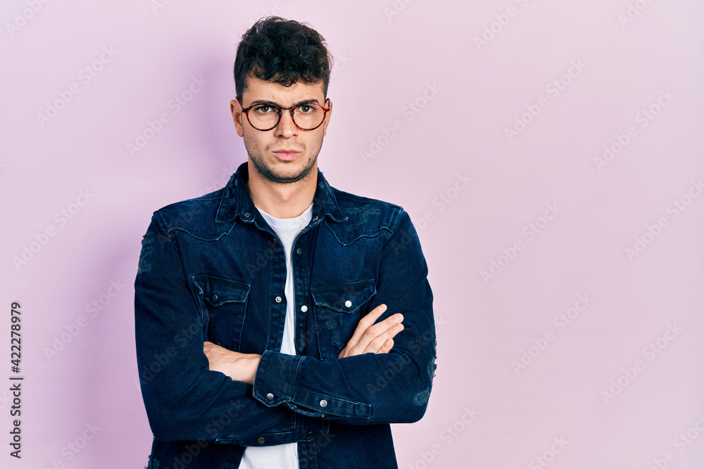 Young hispanic man wearing casual clothes and glasses skeptic and nervous, disapproving expression on face with crossed arms. negative person. Young hispanic man wearing casual clothes and glasses skeptic and nervous, disapproving expression on face with crossed arms. negative person.