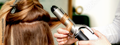 Back view of female hairdresser's hands curling women's hair with curling iron in a hair salon