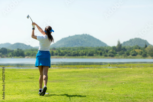 Golfer sport course golf ball fairway. People lifestyle woman playing game golf and hitting go on green grass river and mountain background.  Asia female player game shot in summer.