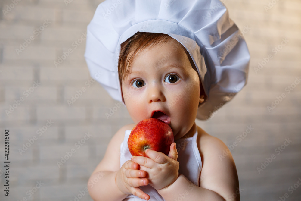 Little boy dressed as a cook in the kitchen. Handsome child dressed in an apron eating an apple Little boy dressed as a cook in the kitchen. Handsome child dressed in an apron eating an apple