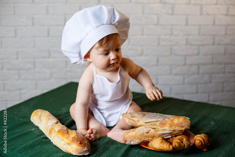 Little boy in a cap and with bread. Little child dressed as a cook in the kitchen. Little boy in a cap and with bread. Little child dressed as a cook in the kitchen.