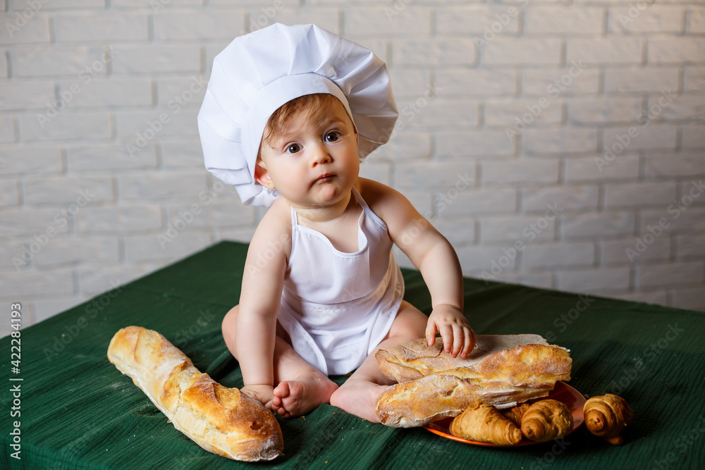 Little boy in a cap and with bread. Little child dressed as a cook in the kitchen. Little boy in a cap and with bread. Little child dressed as a cook in the kitchen.