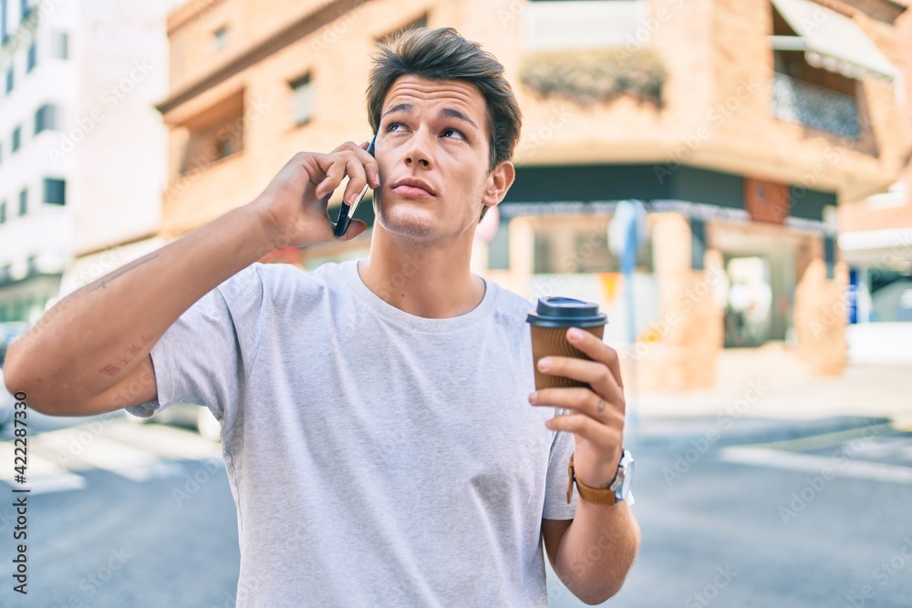 Young caucasian man with serious expression talking on the smartphone and drinking coffee at the city. Young caucasian man with serious expression talking on the smartphone and drinking coffee at the city.