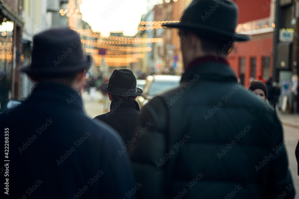 People walking in the city.  3 gentlemen with hats on a weekend.  Focus on the central figure.