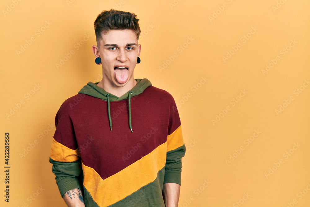Young caucasian boy with ears dilation wearing casual sweatshirt sticking tongue out happy with funny expression. emotion concept. Young caucasian boy with ears dilation wearing casual sweatshirt sticking tongue out happy with funny expression. emotion concept.