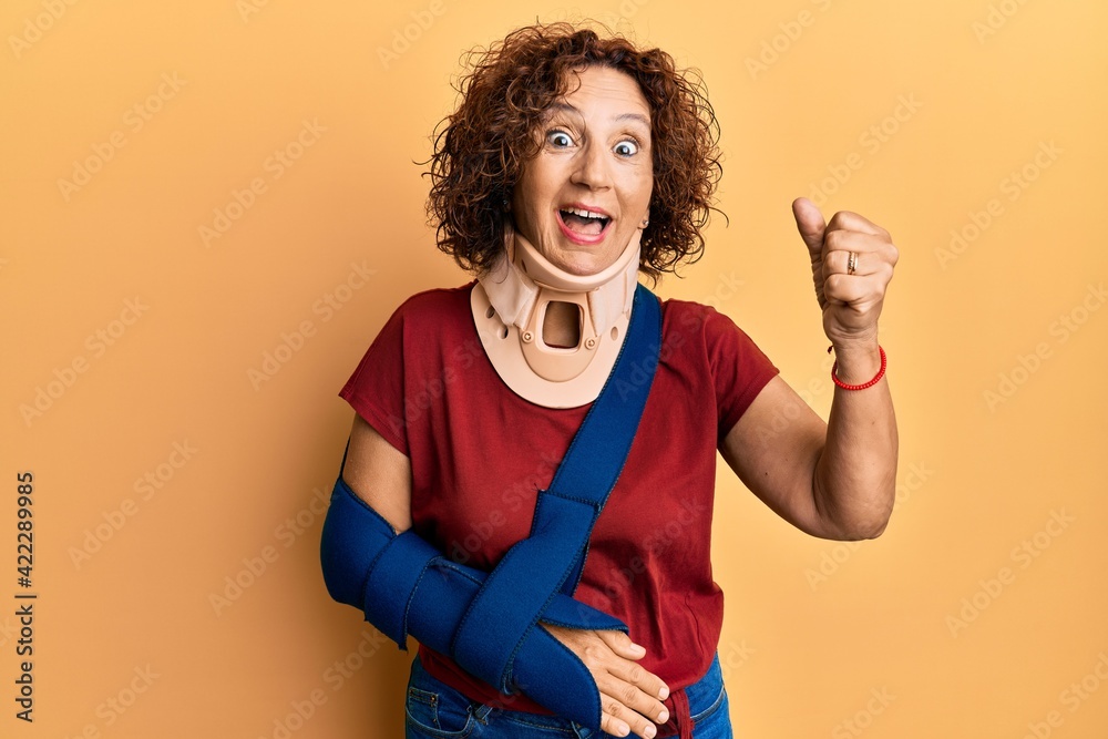 Beautiful middle age mature woman wearing cervical collar and arm on sling screaming proud, celebrating victory and success very excited with raised arms Beautiful middle age mature woman wearing cervical collar and arm on sling screaming proud, celebrating victory and success very excited with raised arms