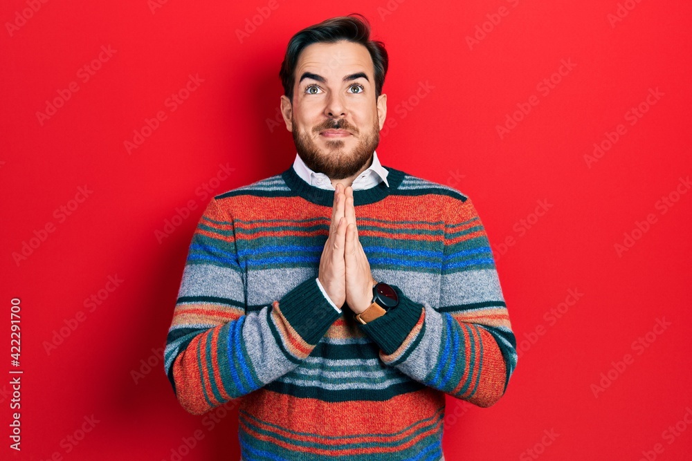 Handsome caucasian man with beard wearing elegant wool winter sweater praying with hands together asking for forgiveness smiling confident. Handsome caucasian man with beard wearing elegant wool winter sweater praying with hands together asking for forgiveness smiling confident.