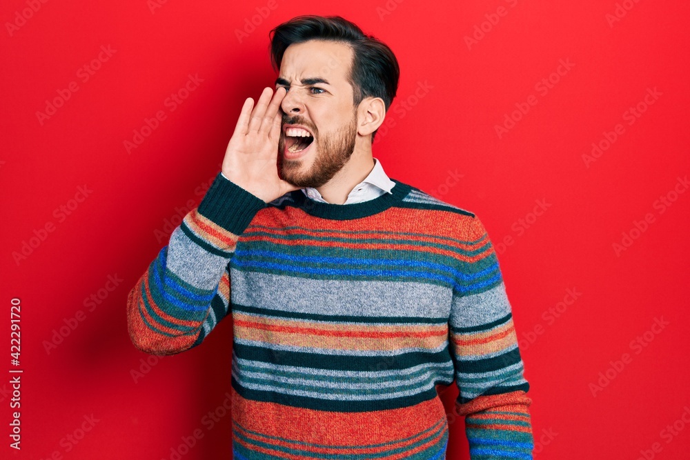 Handsome caucasian man with beard wearing elegant wool winter sweater shouting and screaming loud to side with hand on mouth. communication concept. Handsome caucasian man with beard wearing elegant wool winter sweater shouting and screaming loud to side with hand on mouth. communication concept.
