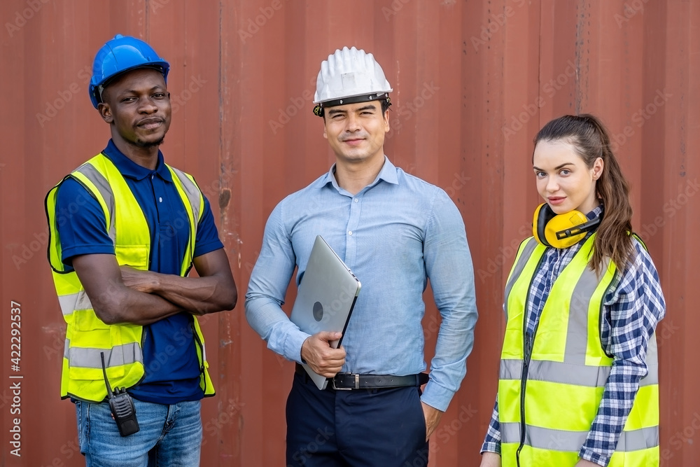 Confident foreman and engineers portrait in uniforms standing in front of the containers. Logistics and shipping, import and export concept Confident foreman and engineers portrait in uniforms standing in front of the containers. Logistics and shipping, import and export concept