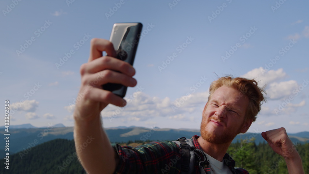 Positive man taking selfie photo on mobile phone in green mountain landscape