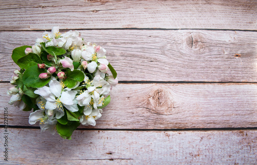 Flower arrangement. A bouquet of spring branches of a blooming apple tree with green leaves and white-pink flowers and buds in a glass of water close-up on a wooden background. Top view. Free space.