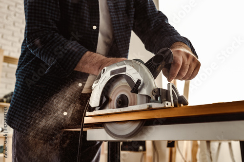 Carpenter hands cutting wood with electrical saw