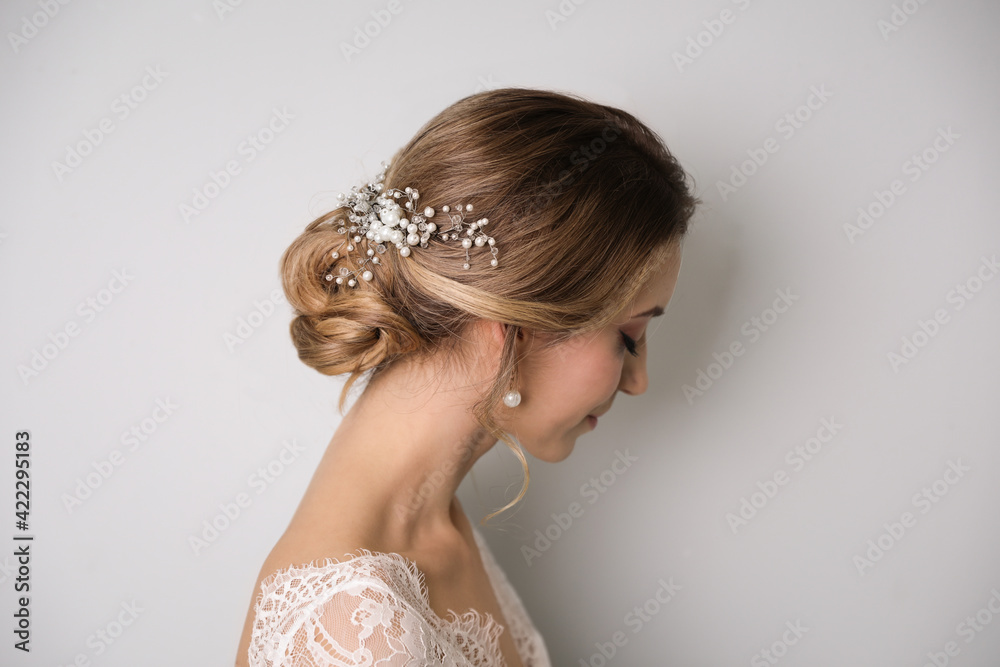 Young bride with elegant wedding hairstyle on light grey background