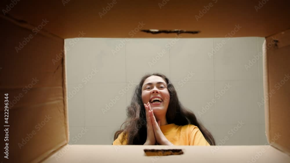 Unpacking. A young happy woman opens a cardboard box and looks at the contents with delight. Bottom view. Product delivery and movement concept