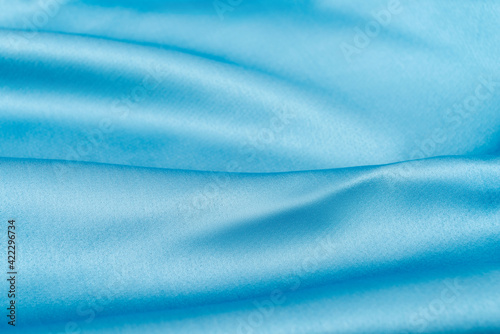 Beautiful wavy silk fabric in sky blue color. Smooth elegant luxury cloth fabric texture. Abstract background design. Copy space, selective focus