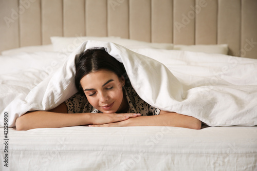 Young woman lying in bed covered with white blanket