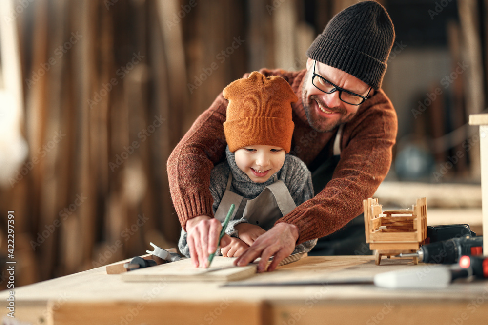 Happy family father and son working together in carpentry workshop - obrazy, fototapety, plakaty 