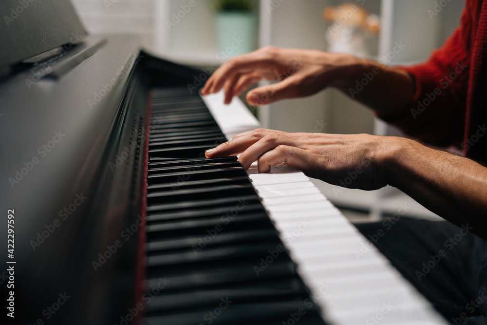 Fototapeta premium Close-up hands of unrecognizable musician man playing on synthesize at home studio. Closeup view of pianist male playing on digital piano in living room. Concept of music education.