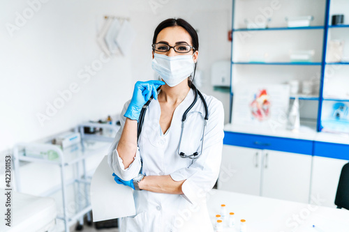 Portrait of a female doctor and her office with a stethoscope  she is smiling and looking at the camera  professional  health and modern medicine