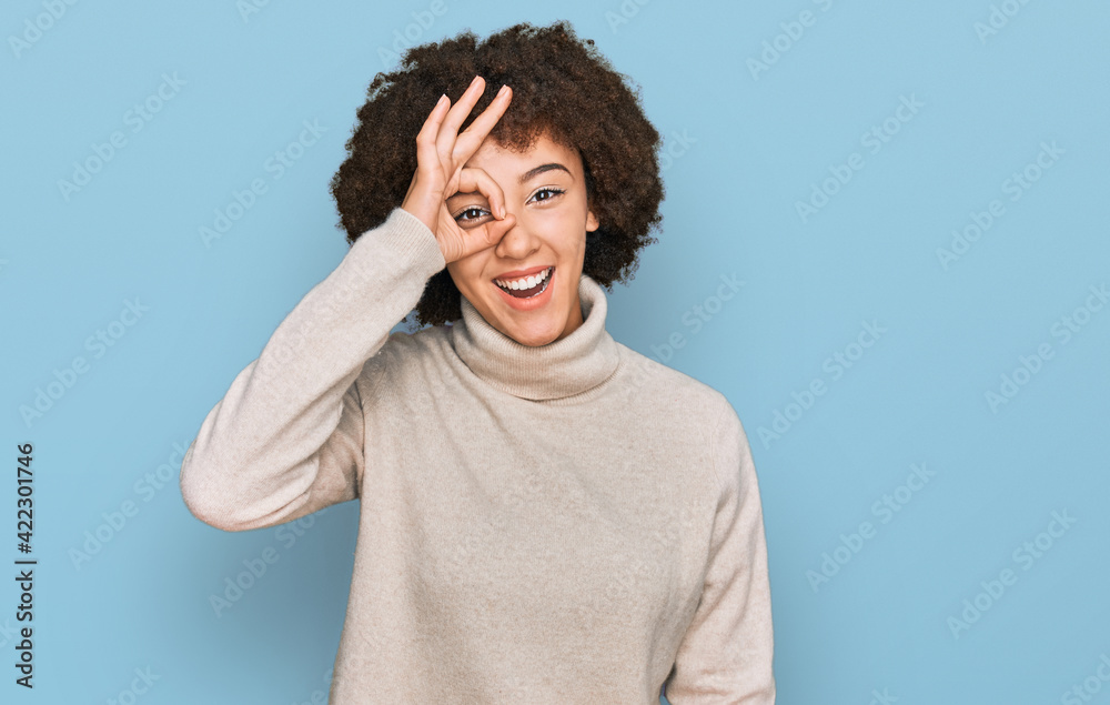 Young hispanic girl wearing wool winter sweater doing ok gesture with hand smiling, eye looking through fingers with happy face. Young hispanic girl wearing wool winter sweater doing ok gesture with hand smiling, eye looking through fingers with happy face.
